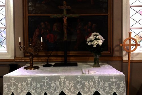 Kustavin kirkon alttaripöytä, jossa valkoinen pitsiliina, valkoisia kukkia maljakossa, krusifiksi ja kynttilä