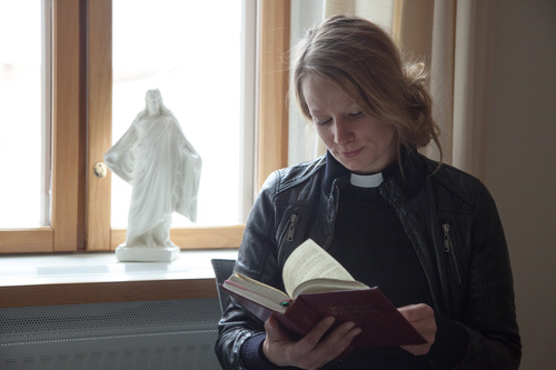 Pappi lukee kirjaa ikkunan ääressä. Ikkunalaudalla on valkoinen Jeesuksen patsas.