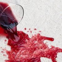 Lattialle kaatunut viinilasi, josta valuu viiniä matolle.
