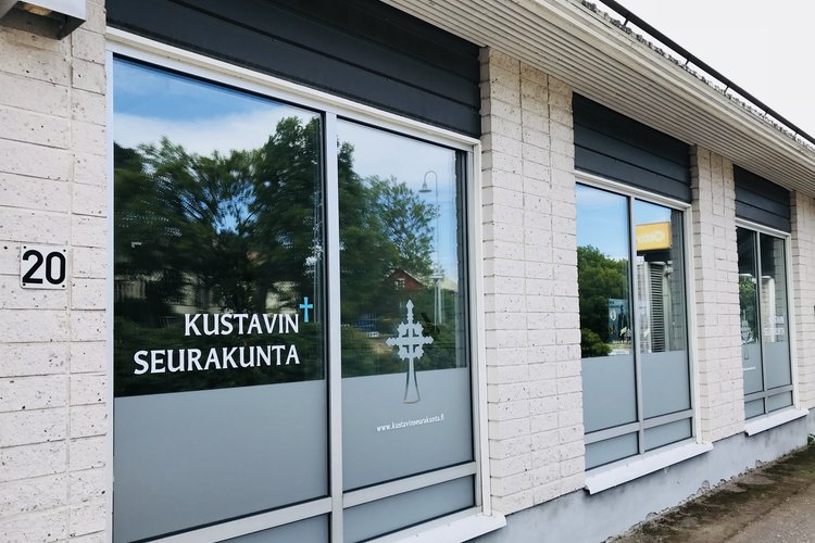 Vaaleatiilinen rakennus, jossa isot ikkunat. Kustavin seurakunnan nimi ja aurinkoristi.