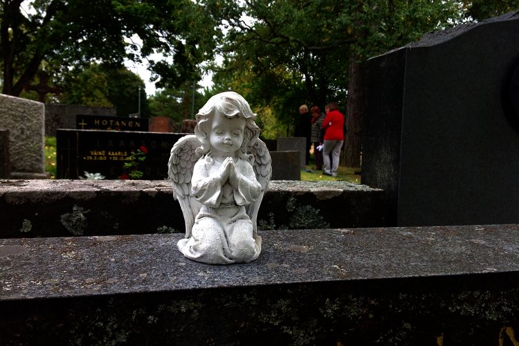 Valkoinen, rukoileva enkelipatsas hautakivellä